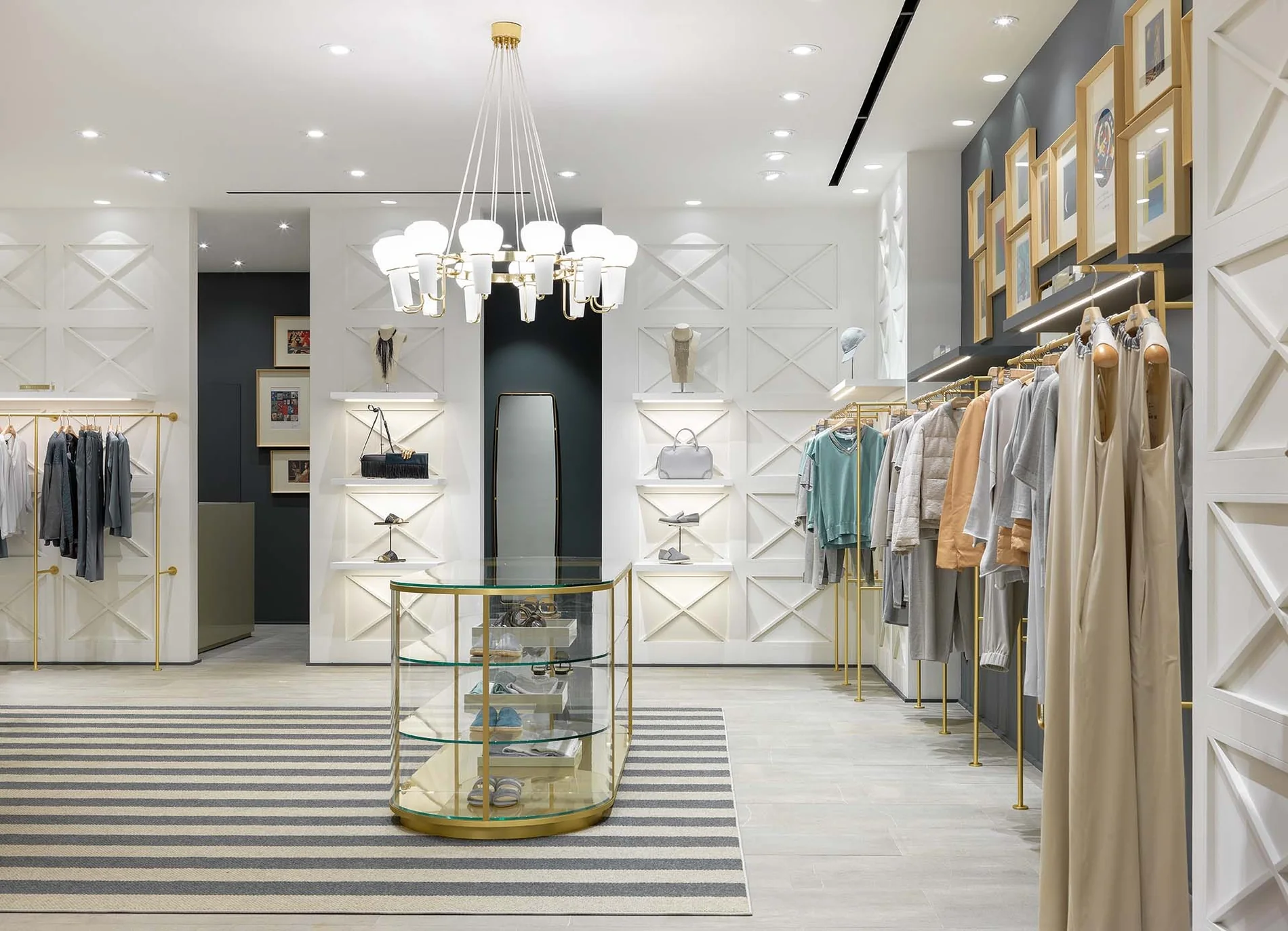 Corredor de una boutique en Moscú, Rusia, con prendas claras, luminarias decorativas y una pared de obras enmarcadas.