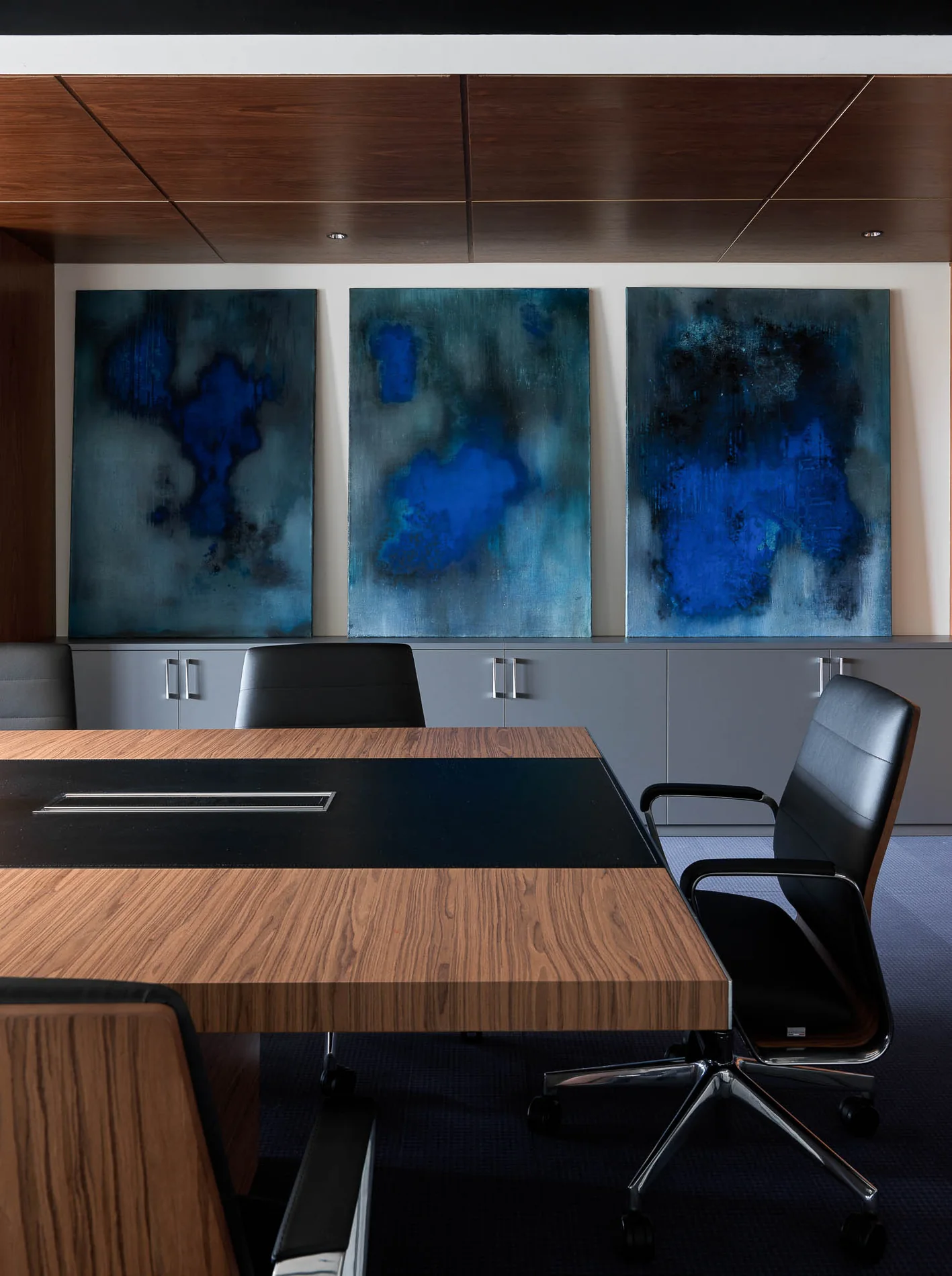 Sala de una oficina en Moscú, Rusia, con mesa de madera y un tríptico abstracto azul.