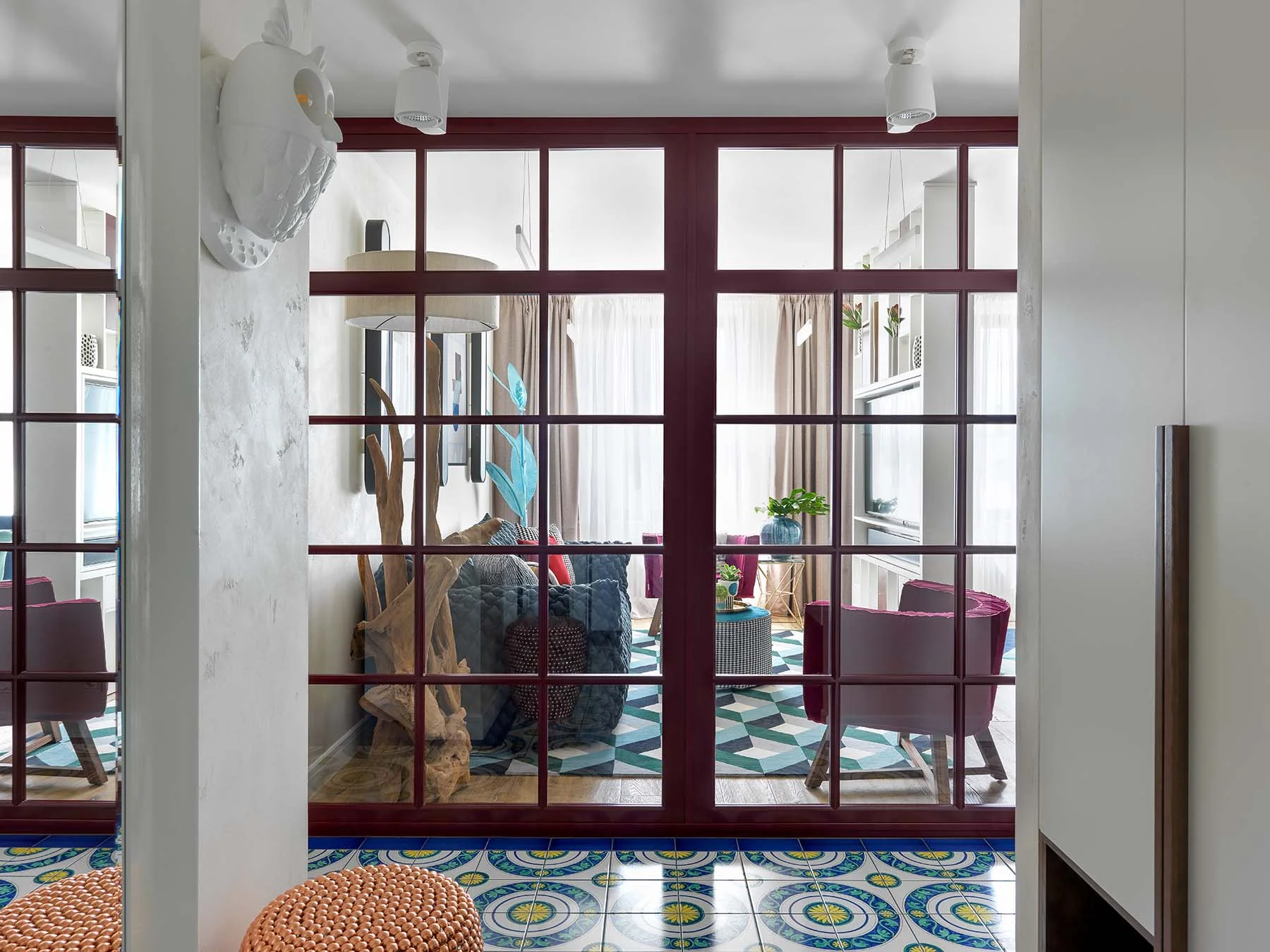 Apartamento en Moscú visto a través de puertas de vidrio burdeos, con textiles y arte de colores intensos.