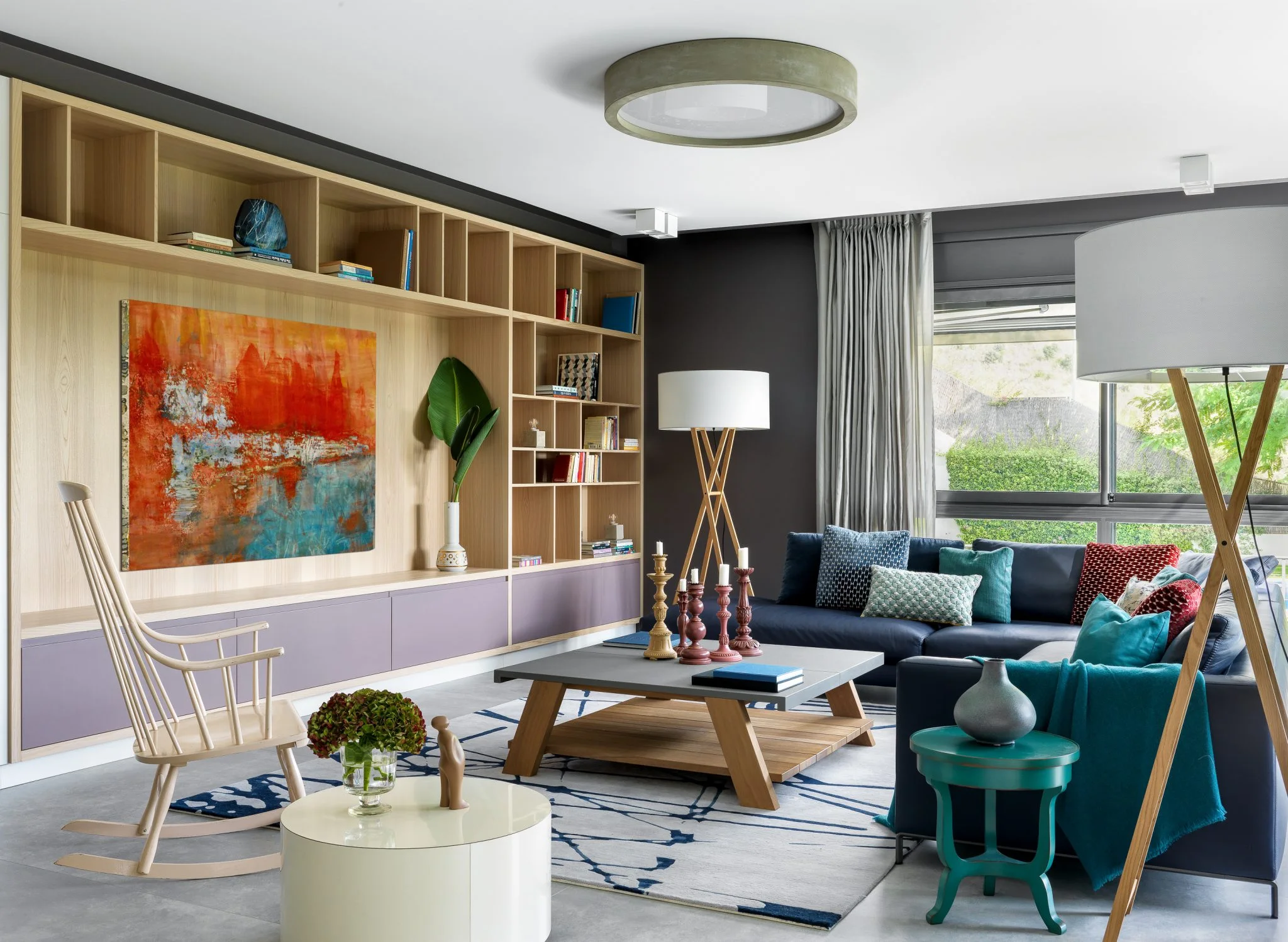 Vista amplia de una vivienda en Barcelona con pintura abstracta naranja y azul, biblioteca de madera y sofá en L.