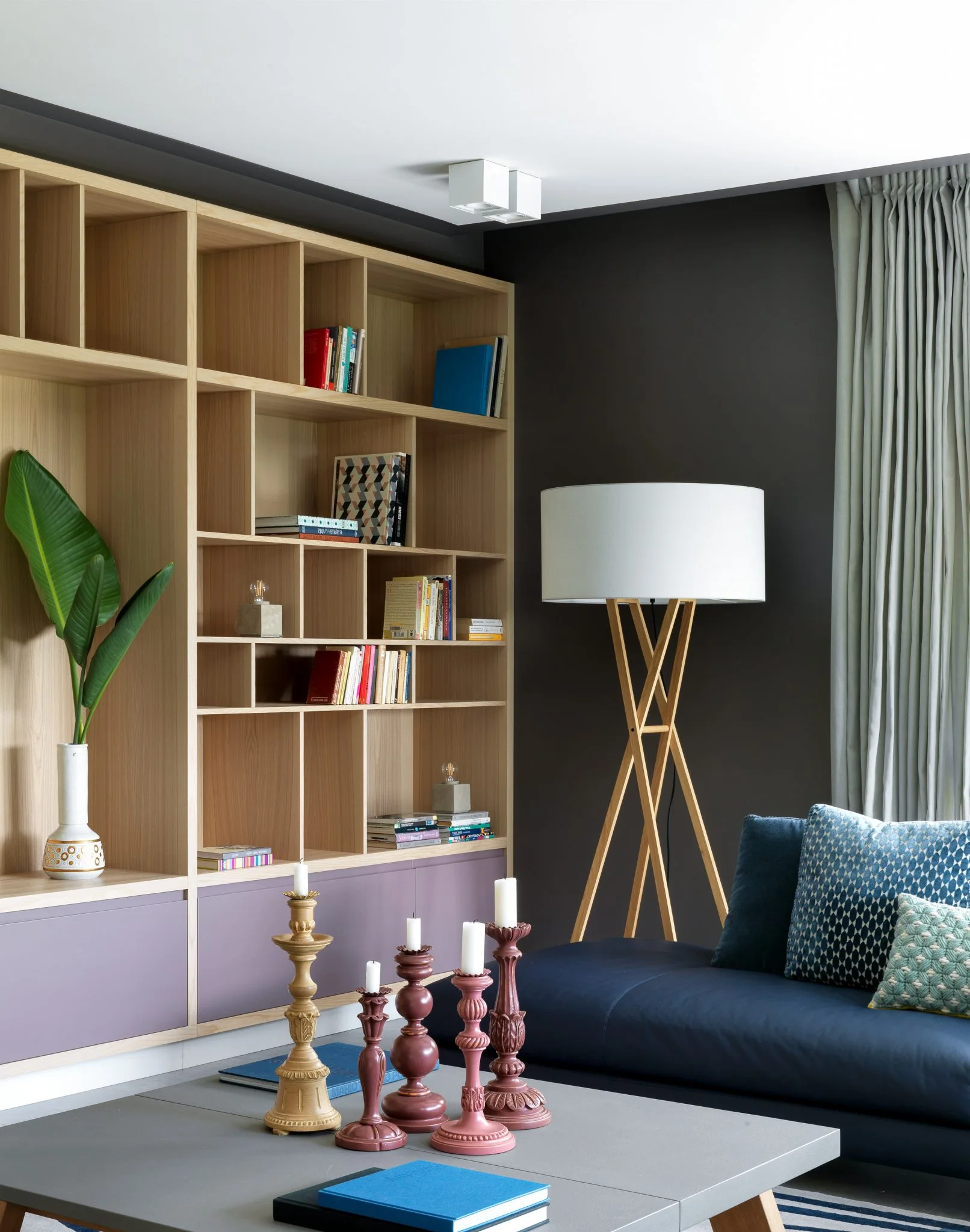 Biblioteca de madera y lámpara de pie junto a un sofá azul en una vivienda de Barcelona.